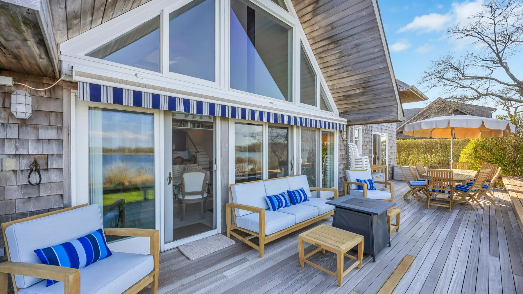 A deck beside a house features outdoor seating and a table facing the water.