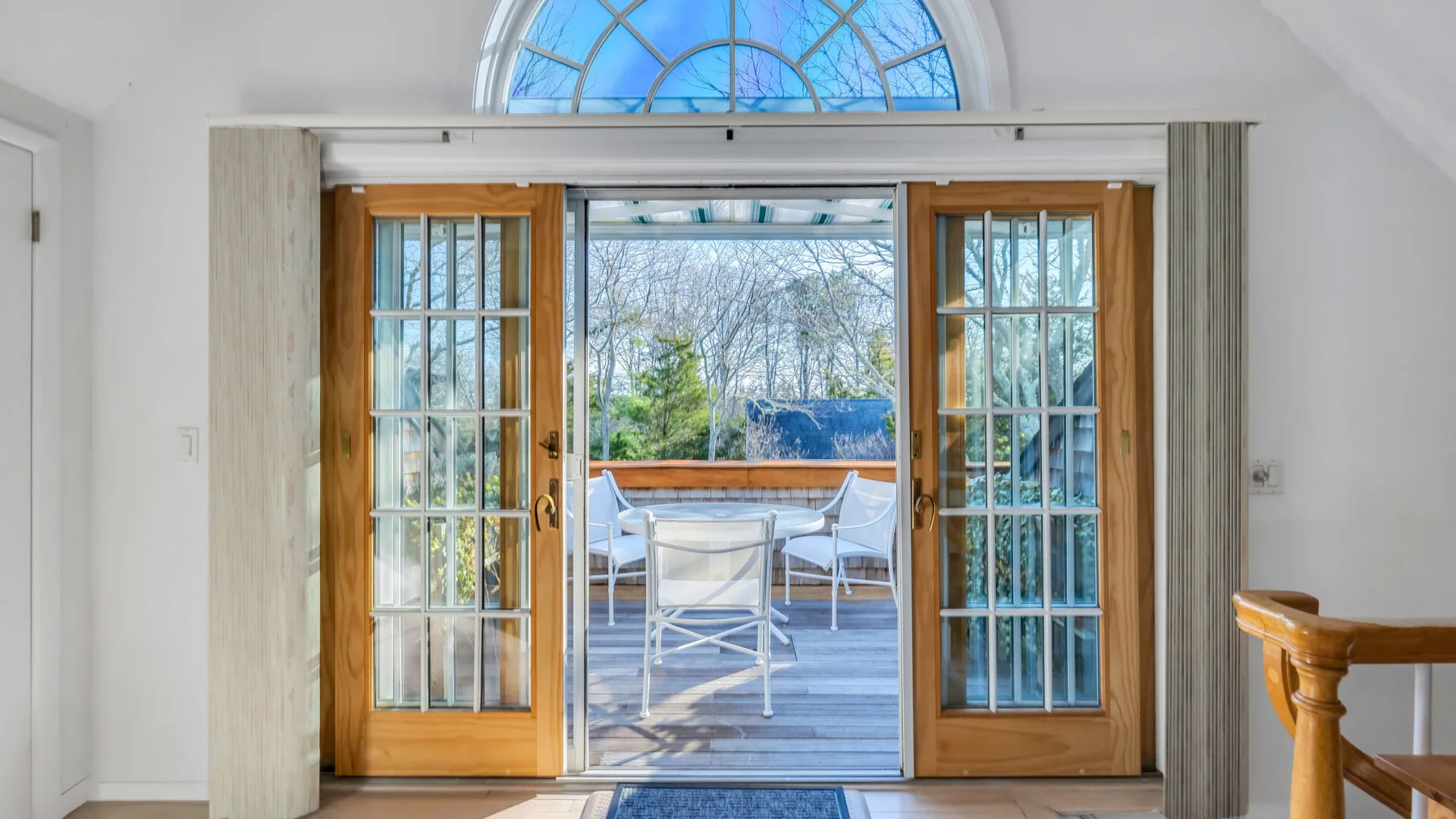 An open doorway leads to a deck with outdoor seating and trees beyond.