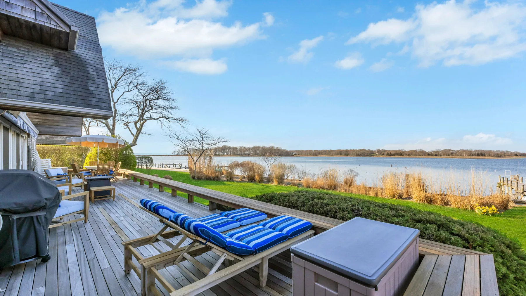 A lakeside deck features striped lounge seating and a view across the water.