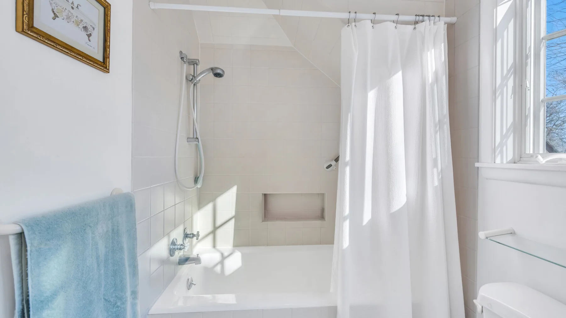 A bright bathroom with a bathtub, shower, and white curtain.