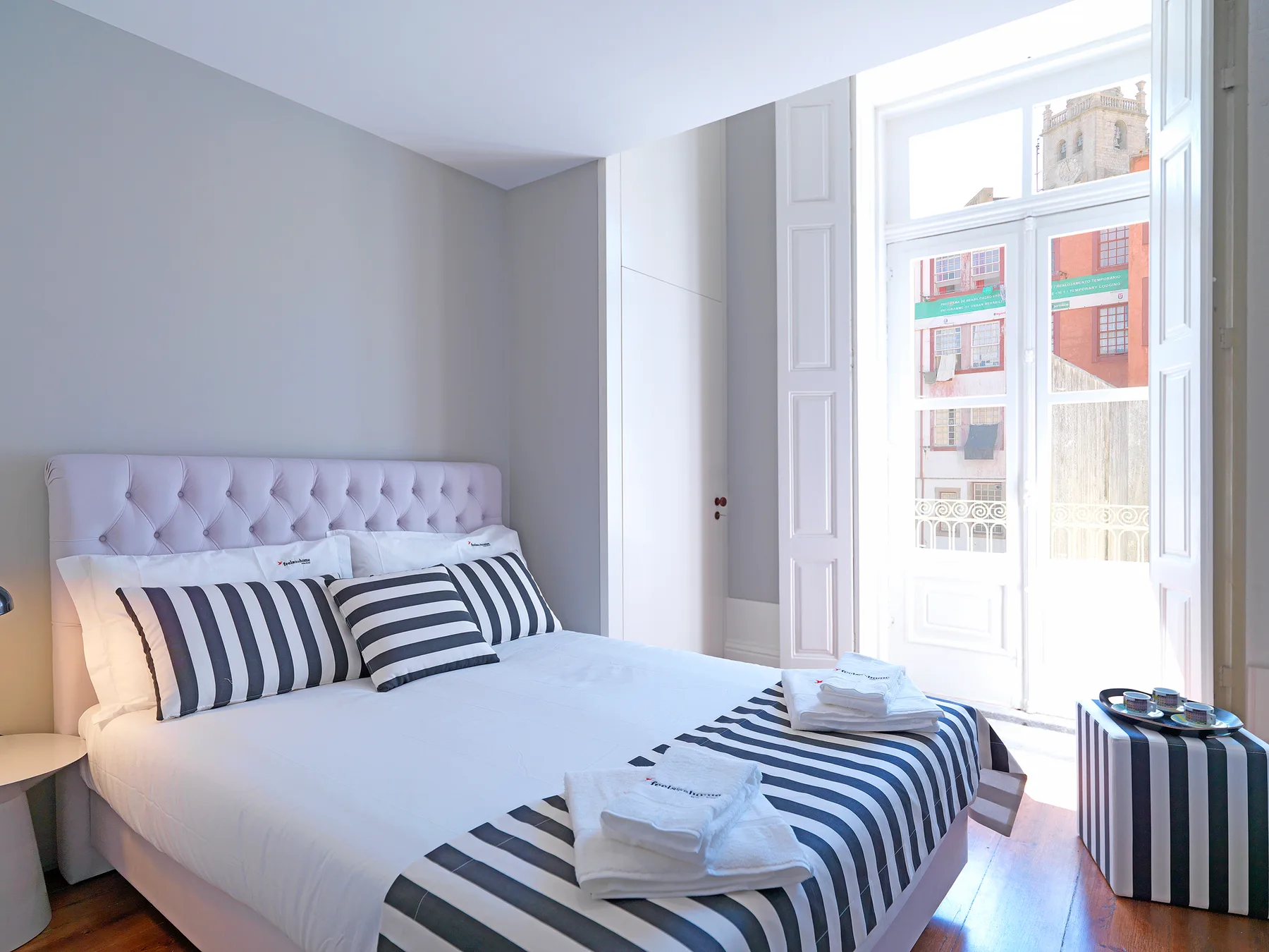 A bright bedroom with a neatly made bed beside tall windows.
