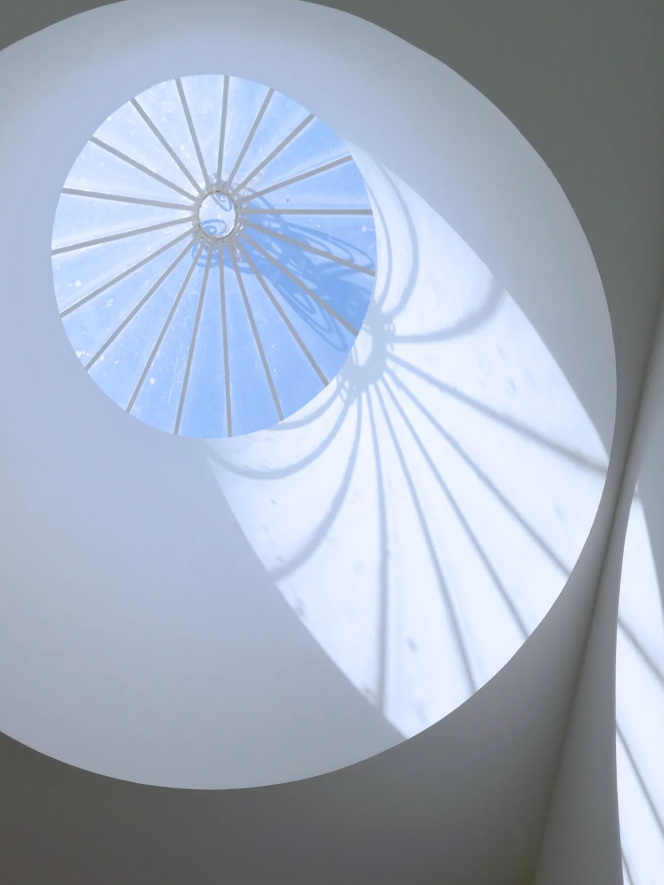 A bright interior stairwell with a circular skylight casting shadows on the wall.