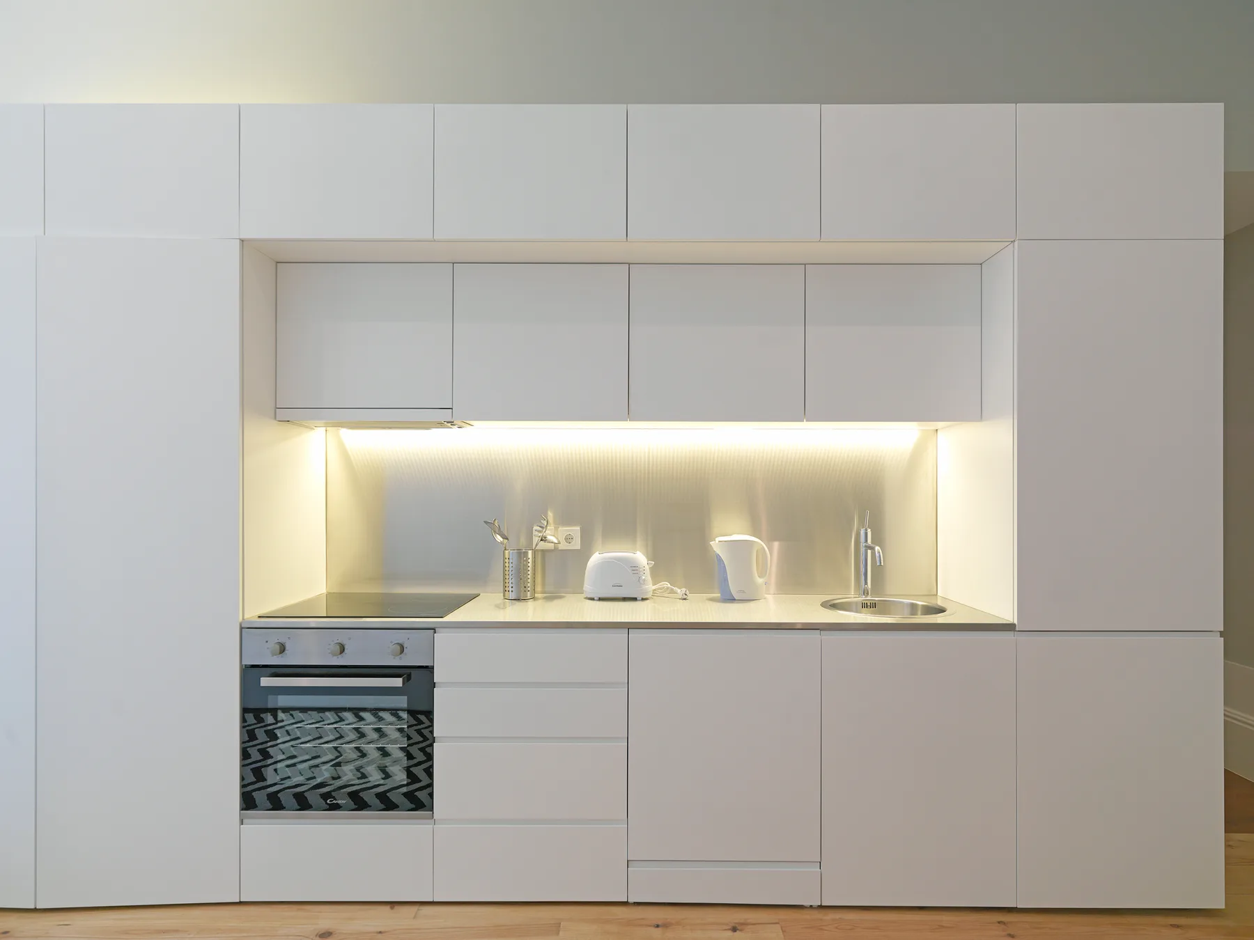 A modern kitchen with white cabinetry, a built-in oven, and a lit countertop.