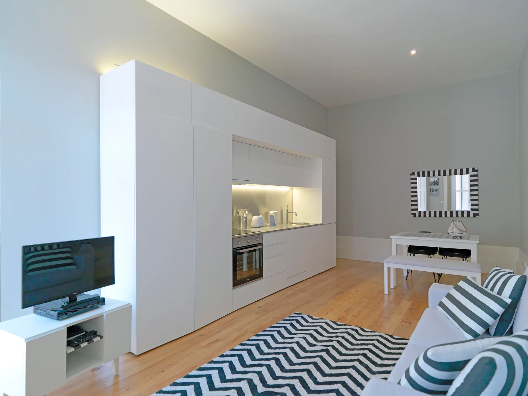A bright living room with a kitchenette, dining table, and striped seating.