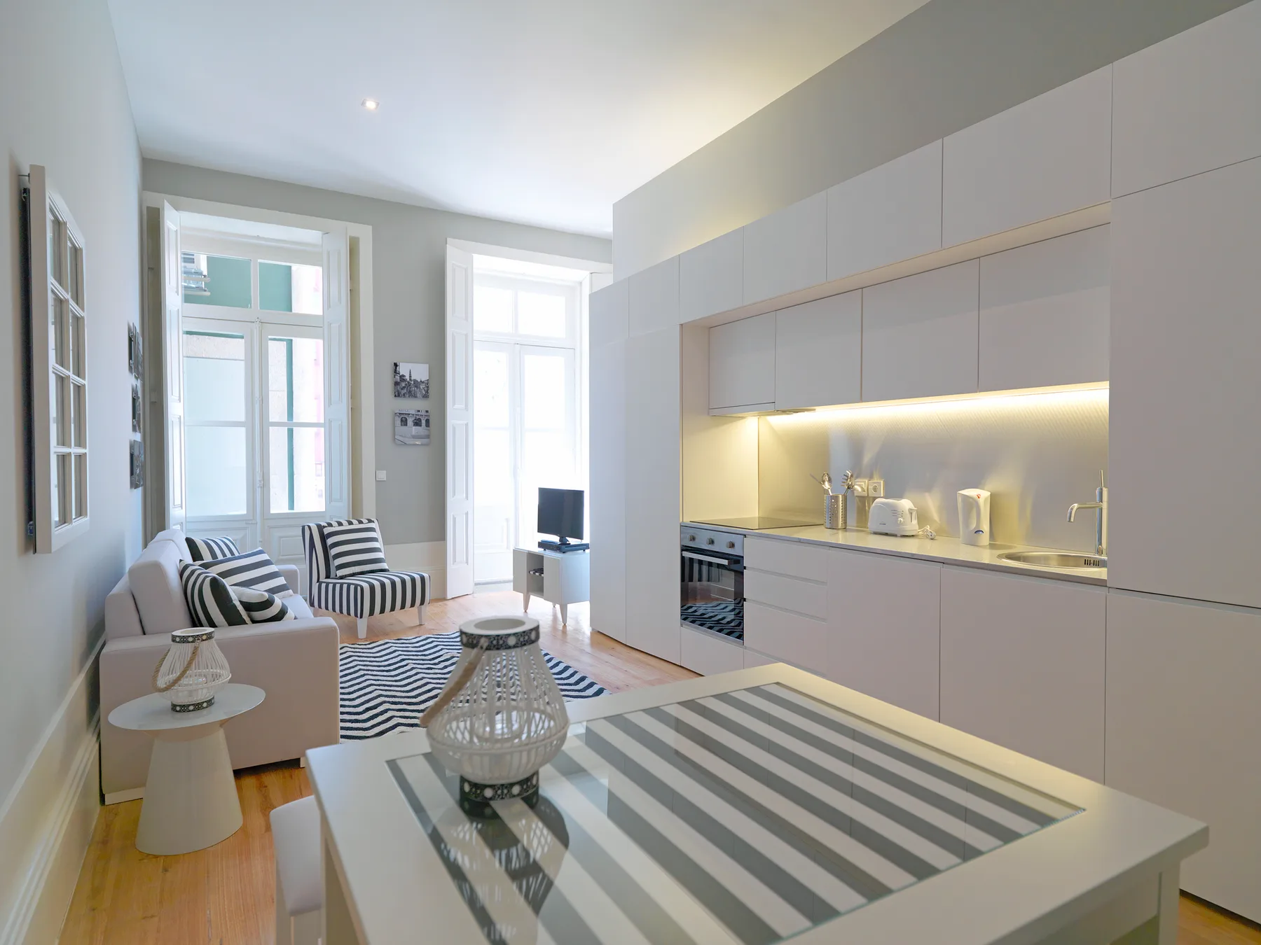 A bright living room with a striped table beside a compact kitchen.