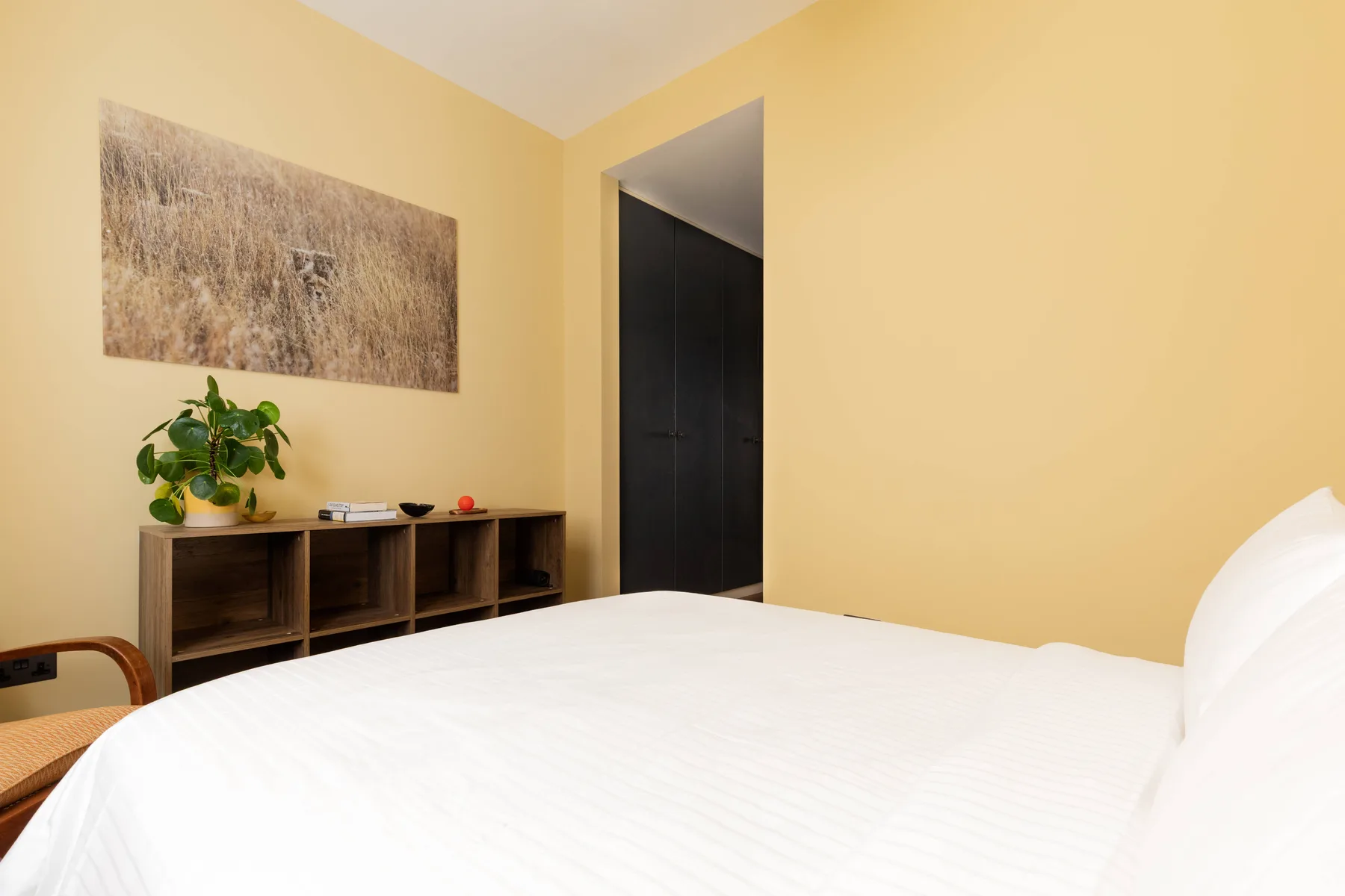 Un dormitorio con una cama bien tendida y un estante bajo bajo un cuadro.