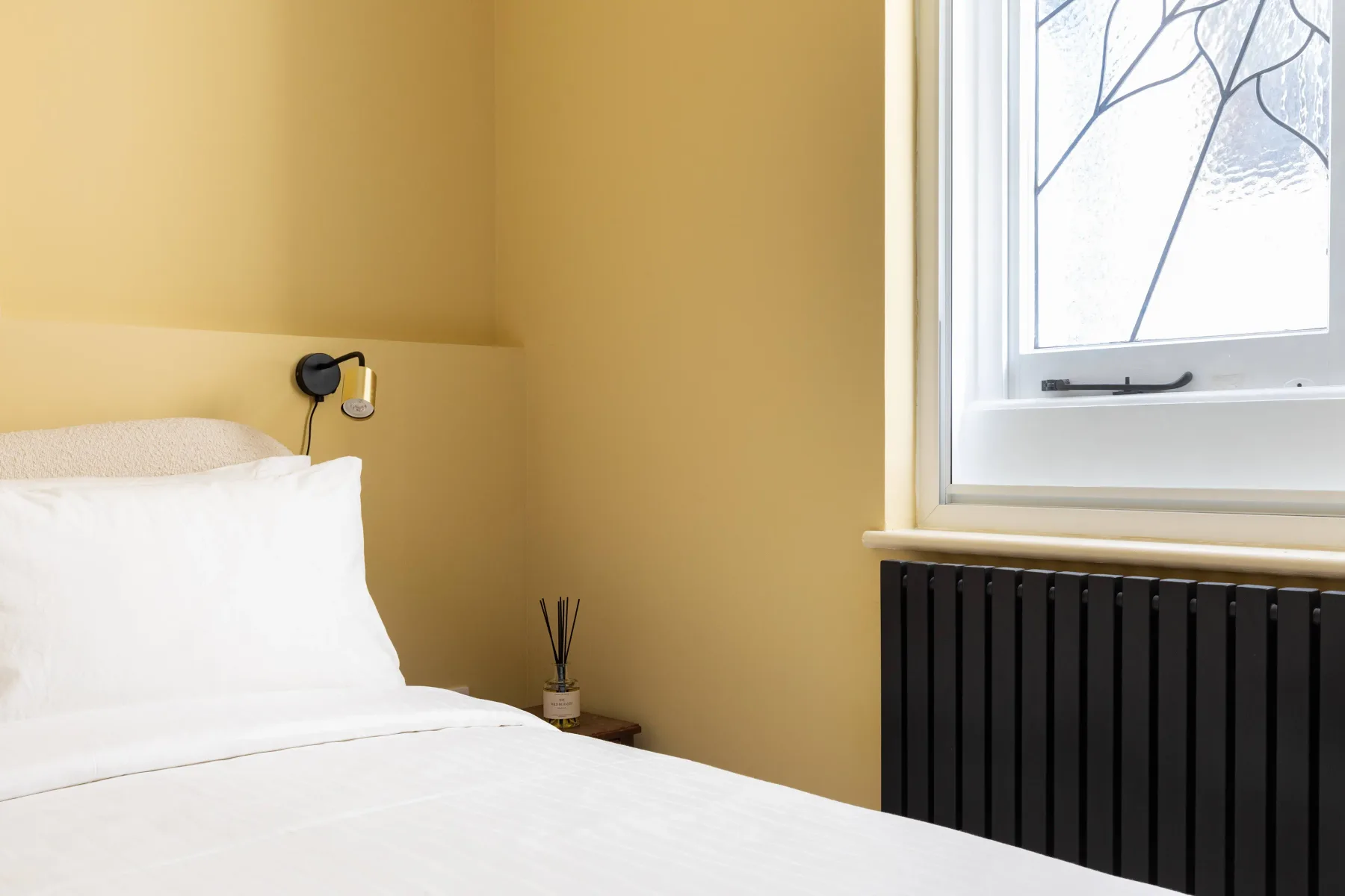 Dormitorio con una cama blanca junto a una ventana y un radiador.