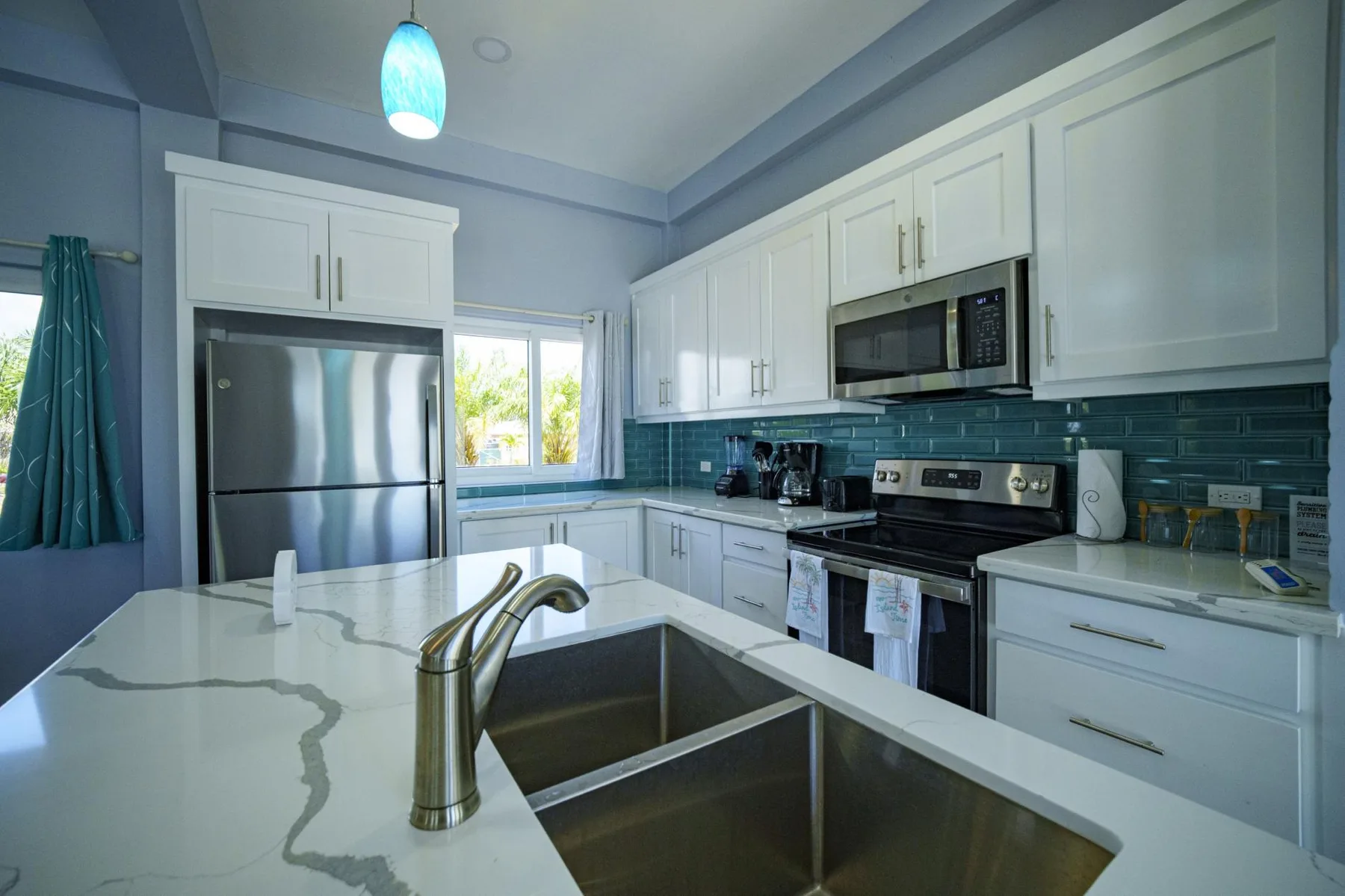 A bright kitchen with white cabinets, stainless steel appliances, and a large sink.