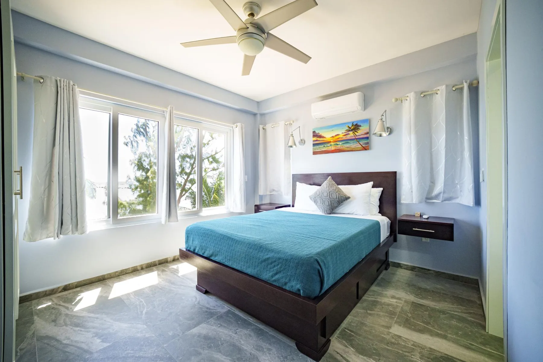 A bedroom with a bed, blue bedding, and windows along the wall.