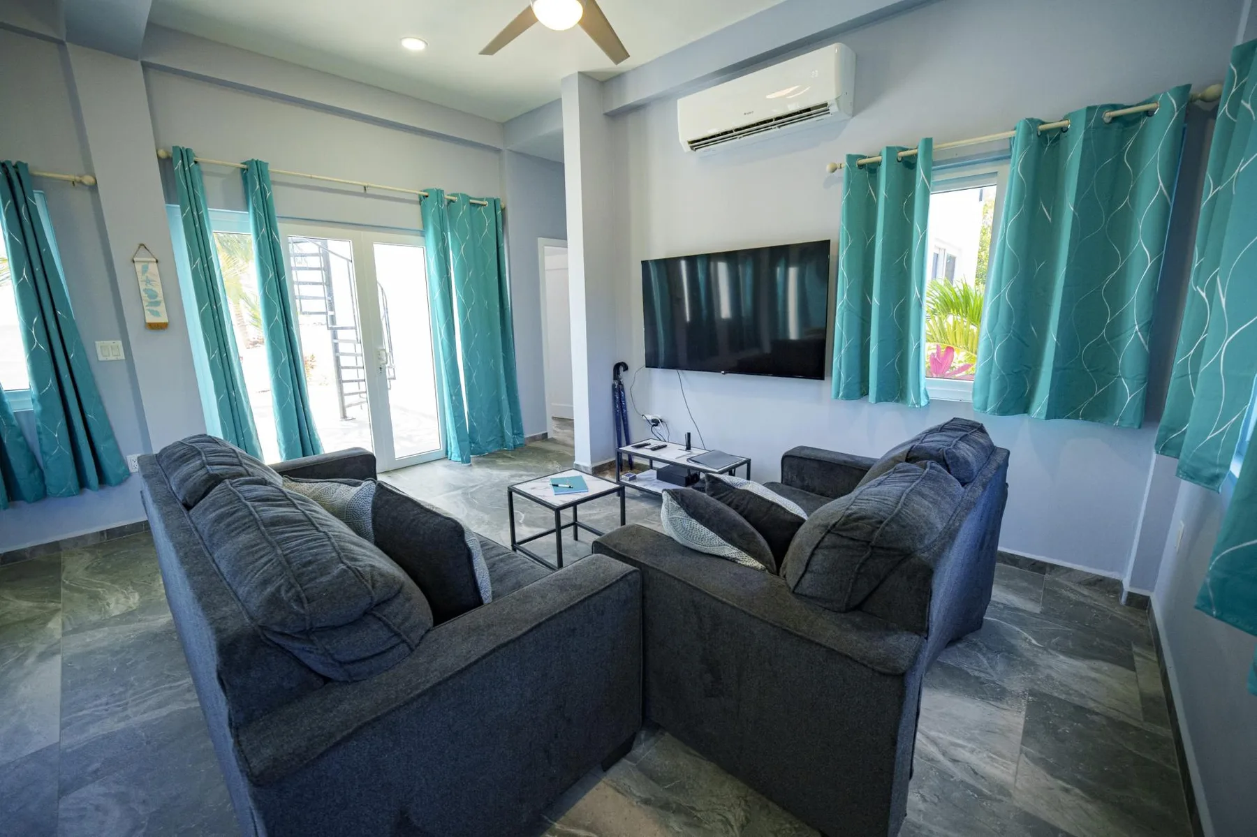 A living room with dark seating, a television, and teal curtains.