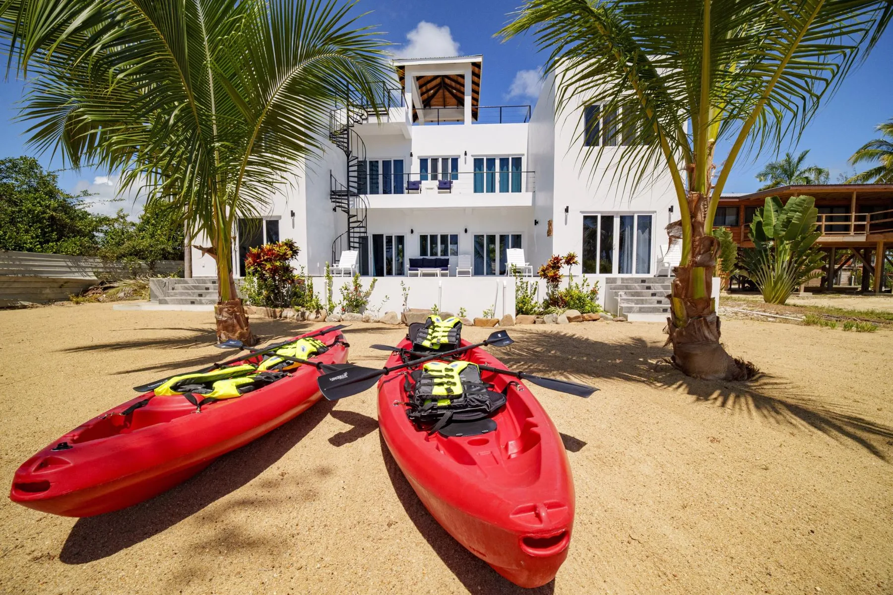 A white multi-story building stands behind two red kayaks on a sandy beach.