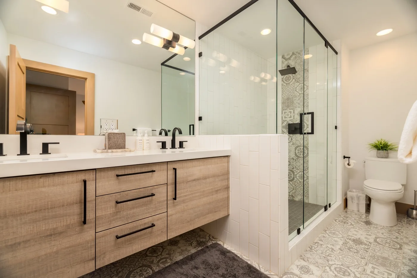 A bright bathroom with a long vanity, double sinks, and a glass shower.