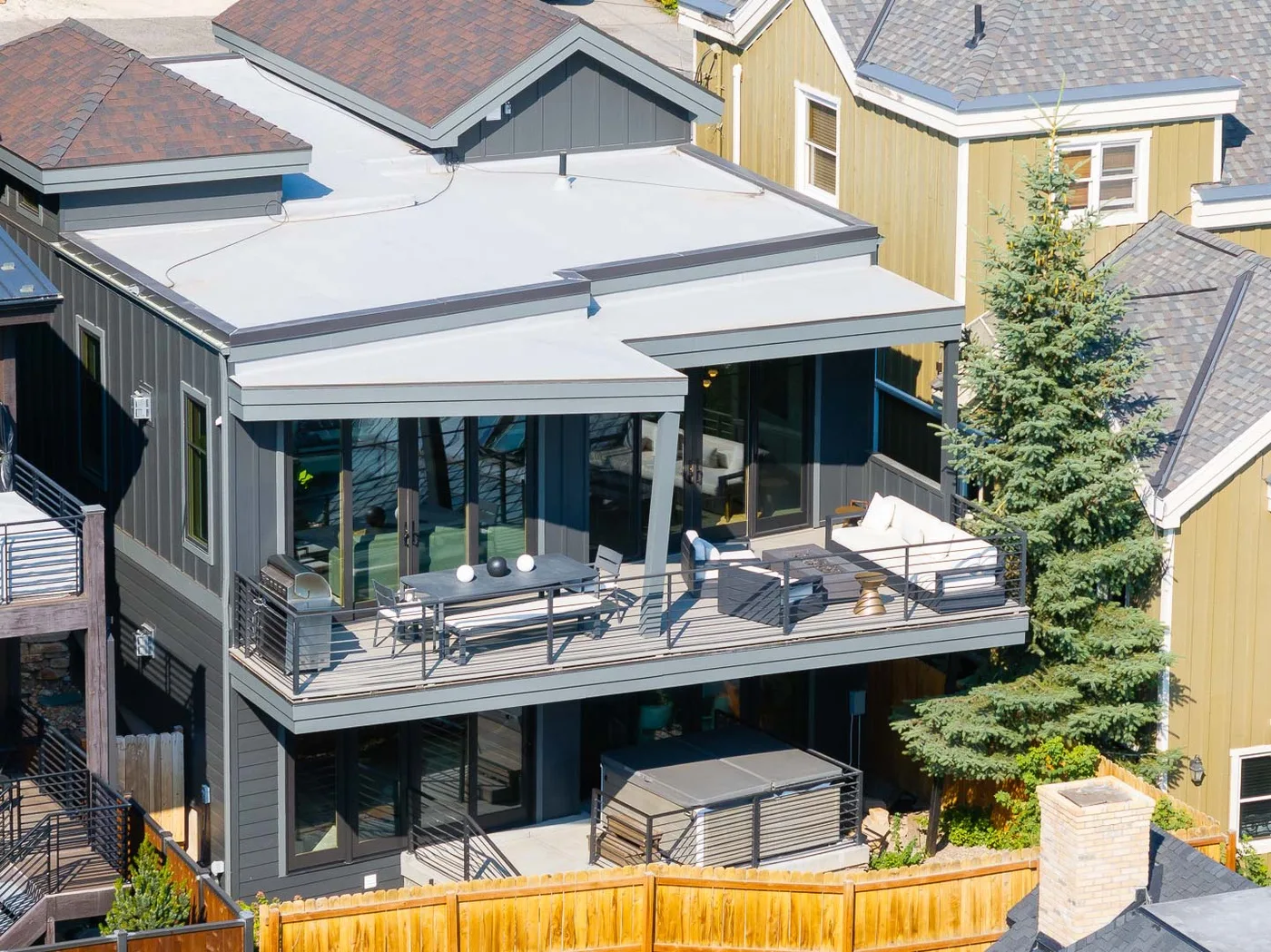 A modern two-story home has a glass-fronted upper deck with outdoor seating.