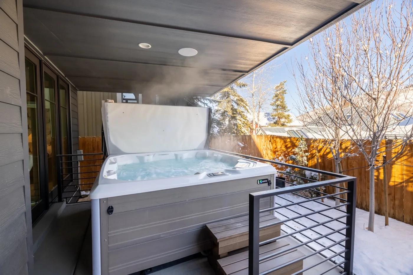 A hot tub sits on a covered outdoor deck beside a railing.
