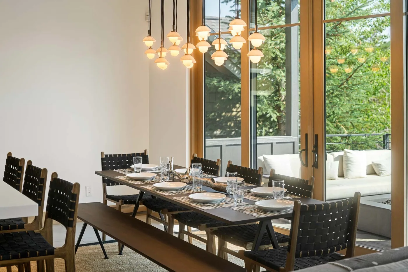 A dining area with a long table and large windows overlooking greenery.