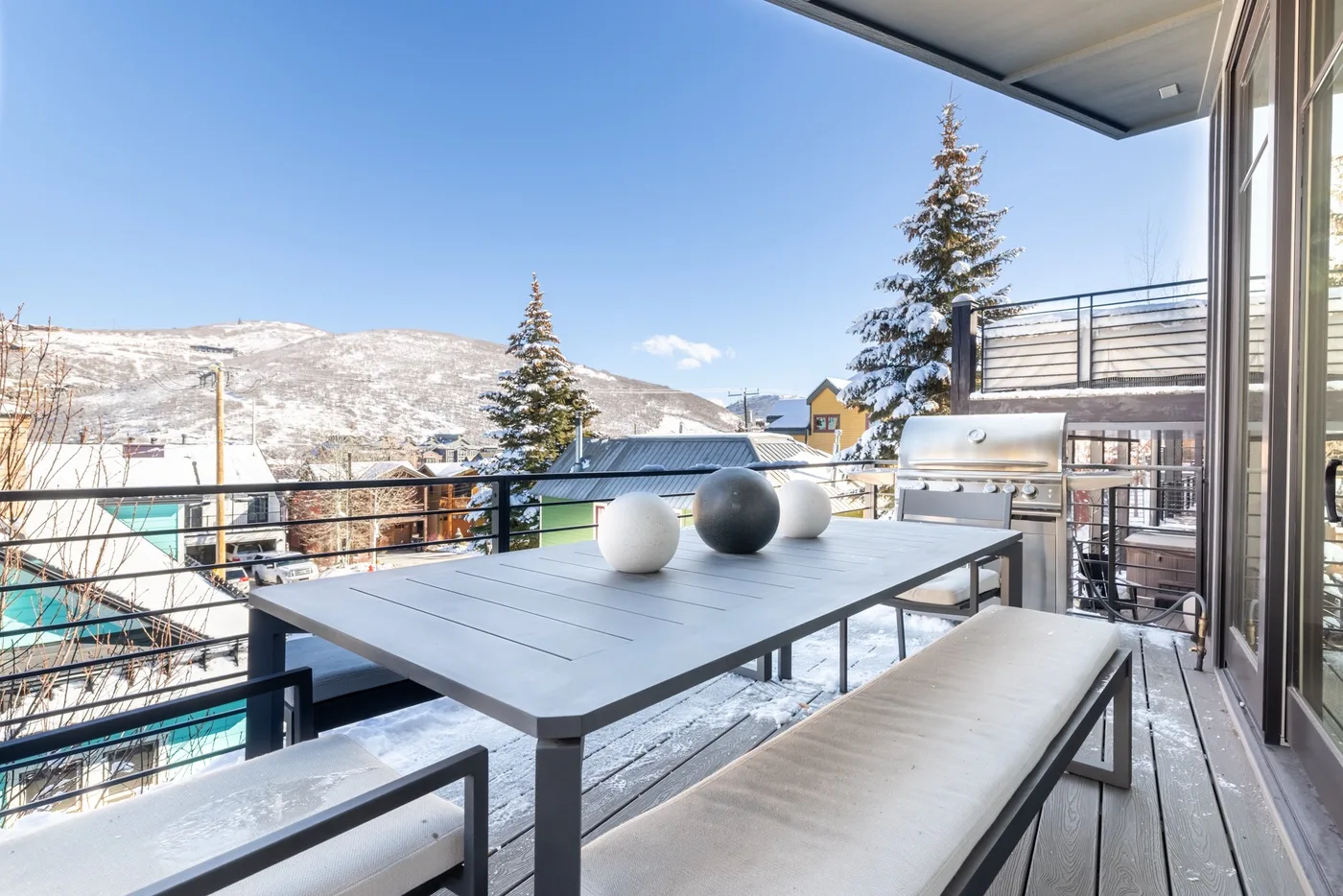 A furnished outdoor terrace overlooks snow-covered hills beneath a clear blue sky.