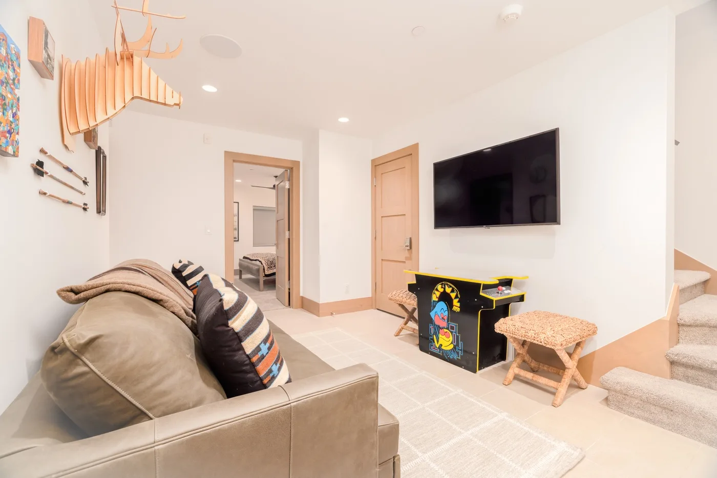 A living room with seating, a wall-mounted television, and a colorful arcade cabinet.