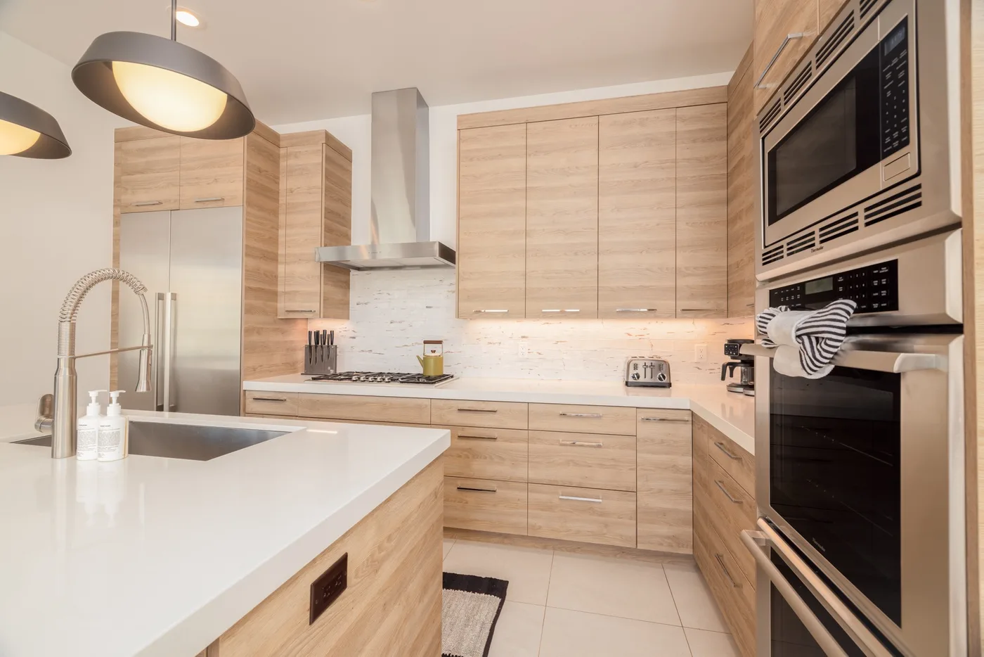A modern kitchen with light wood cabinets, a white counter, and built-in appliances.