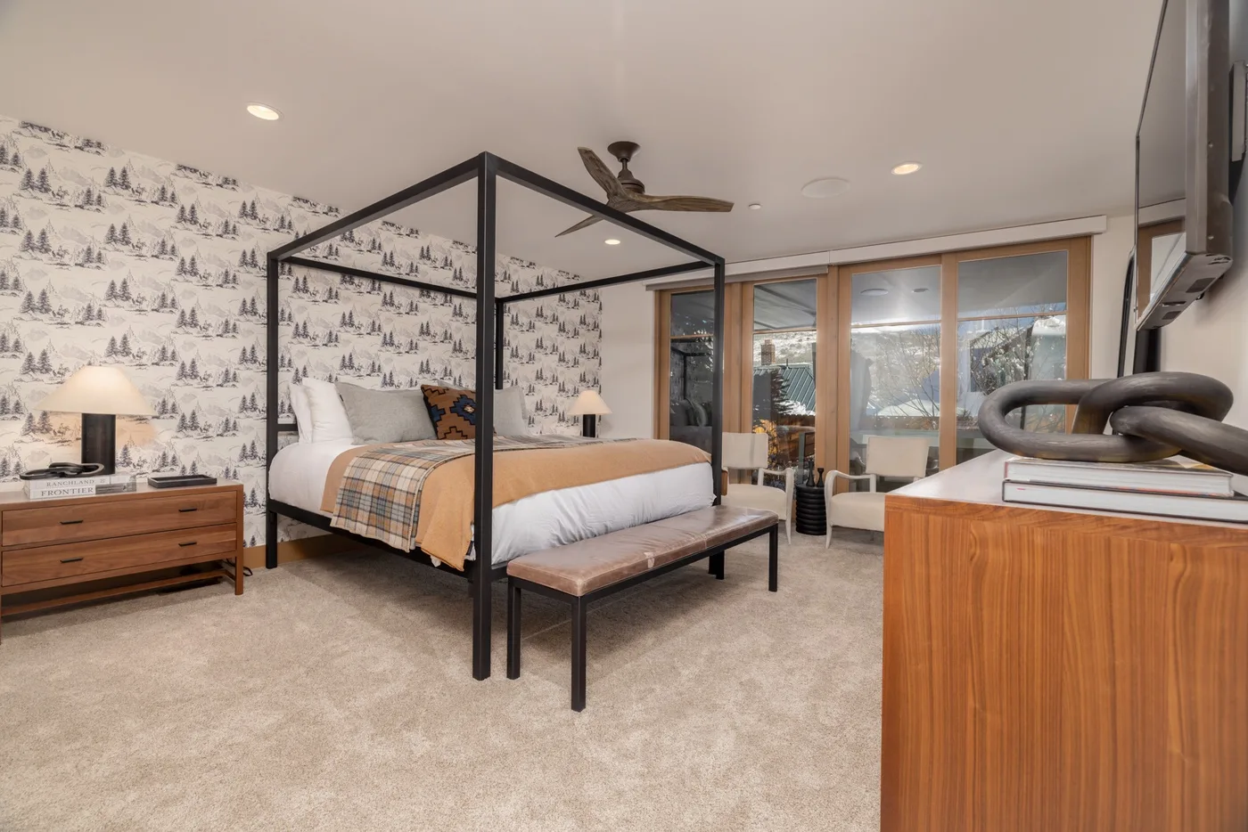 A bedroom with a four-poster bed and patterned wallpaper.