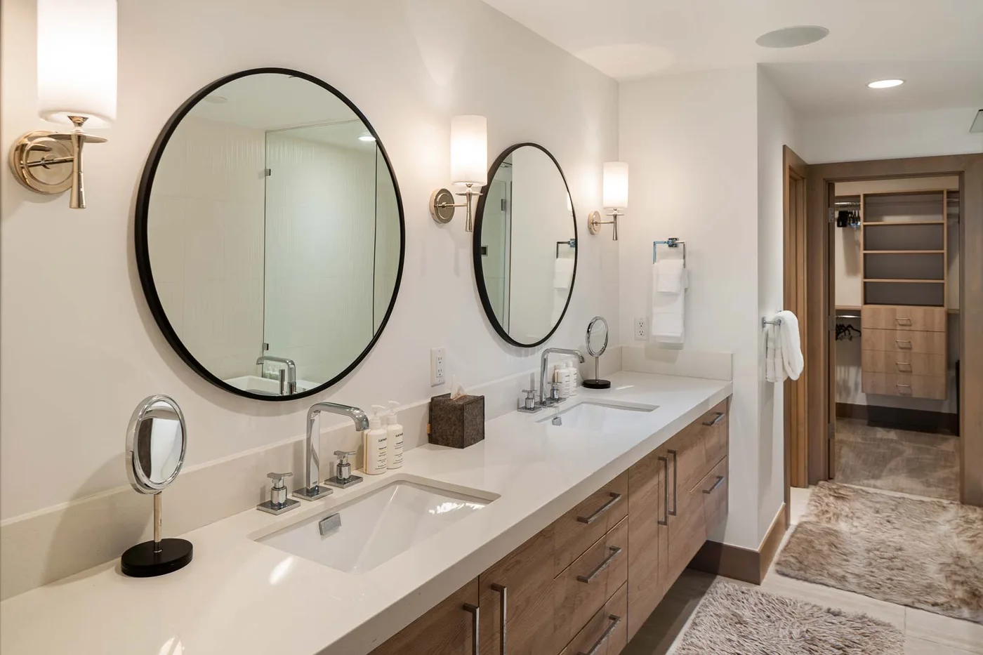 A bright bathroom vanity with two sinks, large mirrors, and a doorway to the adjoining room.