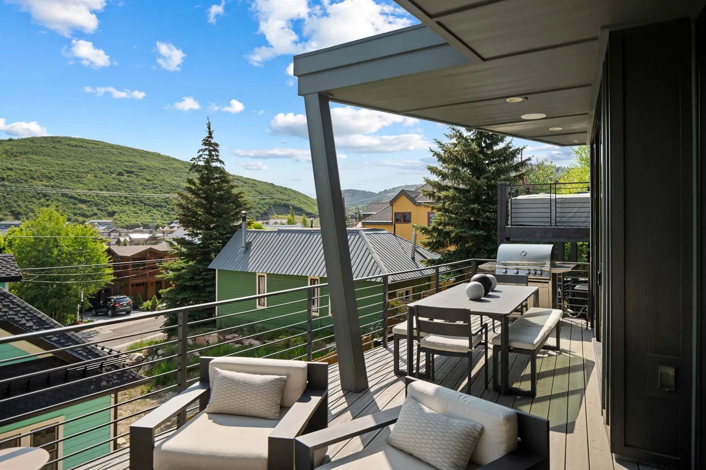 A covered outdoor terrace with seating and a dining table overlooks a green hillside.
