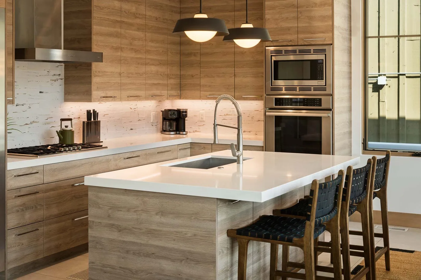 A modern kitchen with wood cabinetry, a central island, and pendant lights.