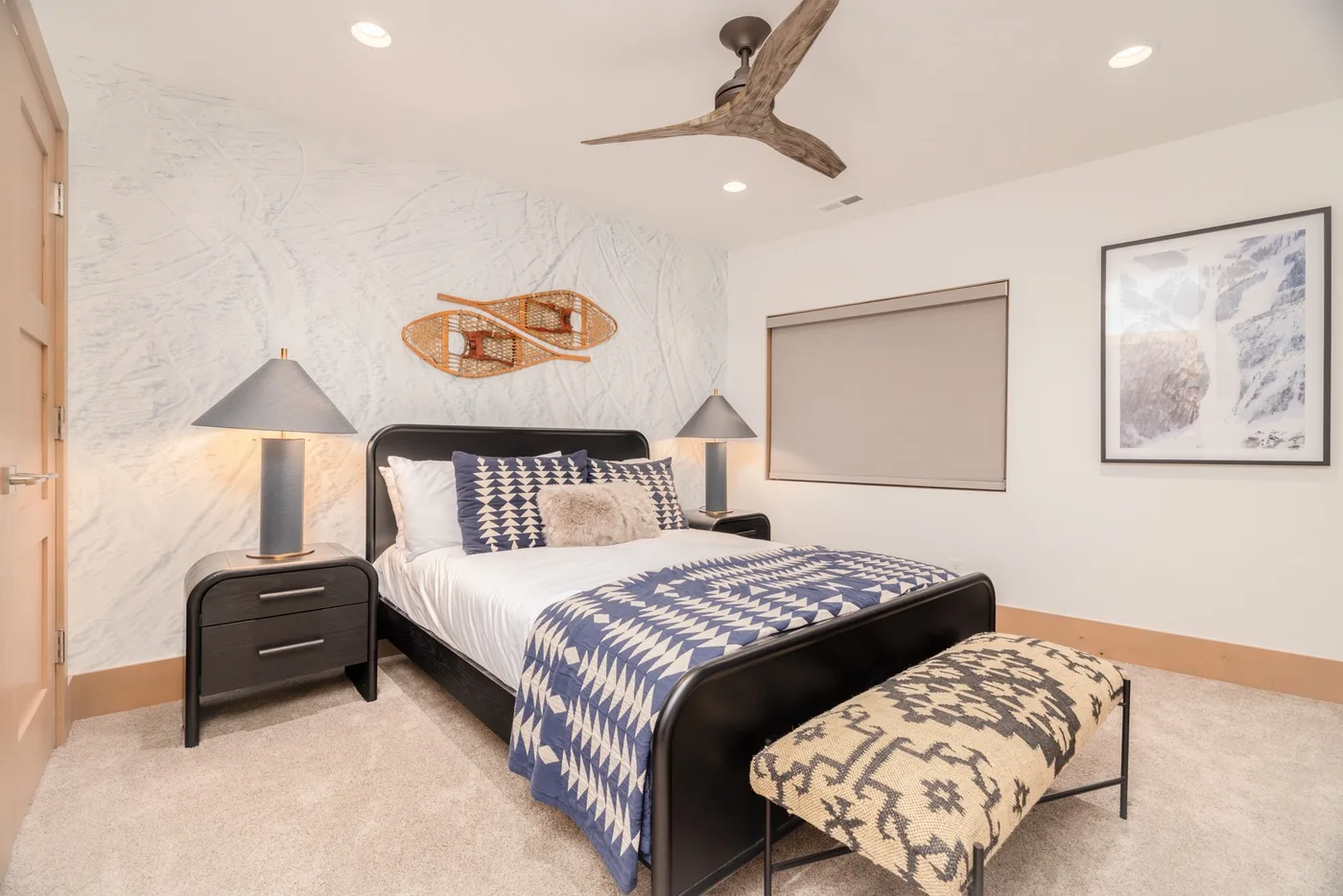 A bedroom with a patterned bedspread, bedside tables, and a ceiling fan.