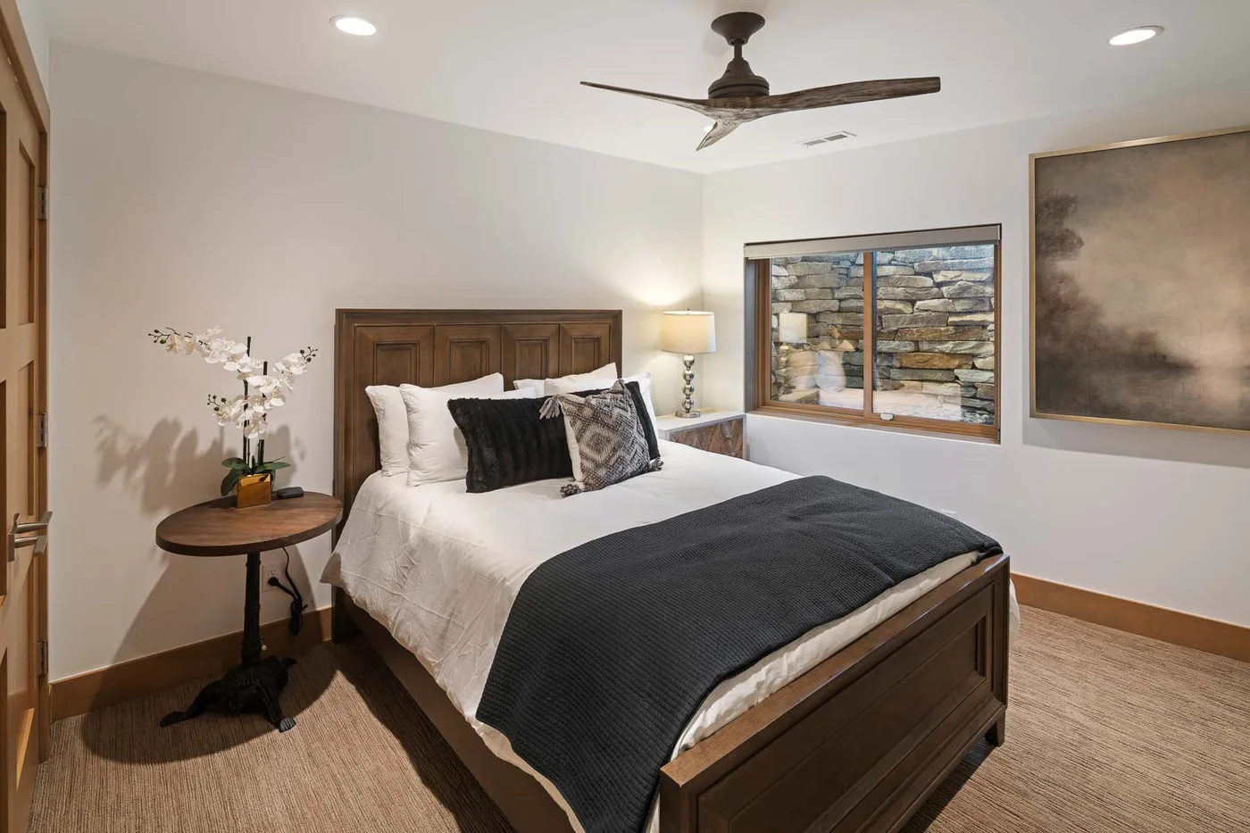 A bedroom with a wooden bed, white bedding, and a dark blanket.