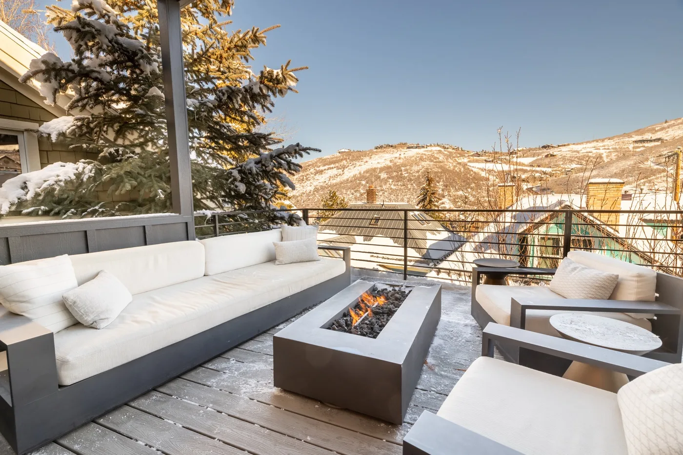An outdoor terrace with seating and a central fire pit overlooks snowy hills.