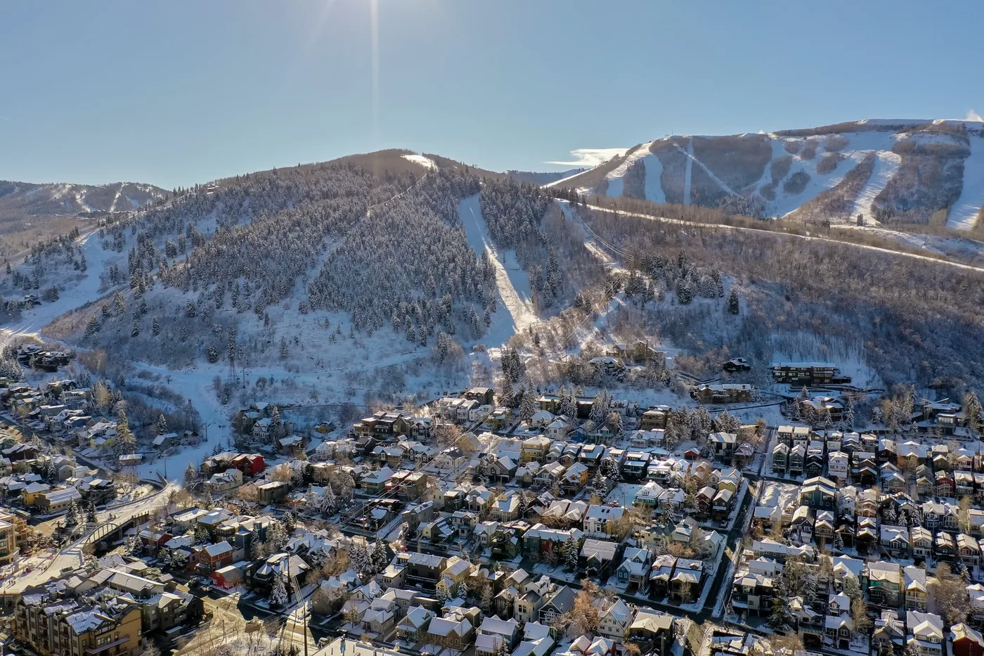 A snow-covered mountain rises behind a village, with ski runs cutting through the slopes.