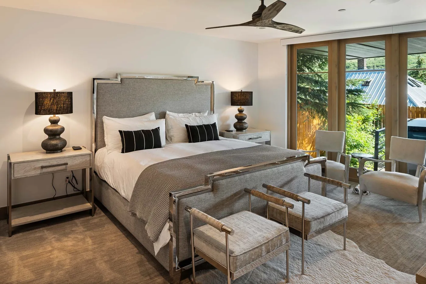 A bedroom with a neatly made bed, bedside tables, and seating by large windows.