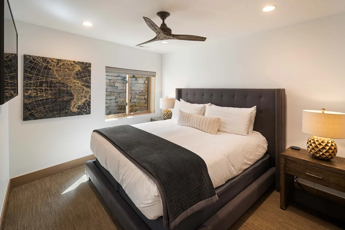 A bedroom with a neatly made bed, dark headboard, and bedside table.