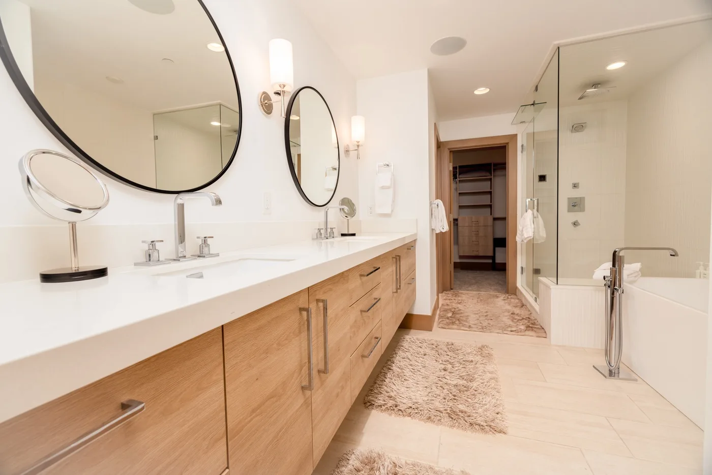 A bright bathroom with a long vanity, large mirrors, and a glass shower.