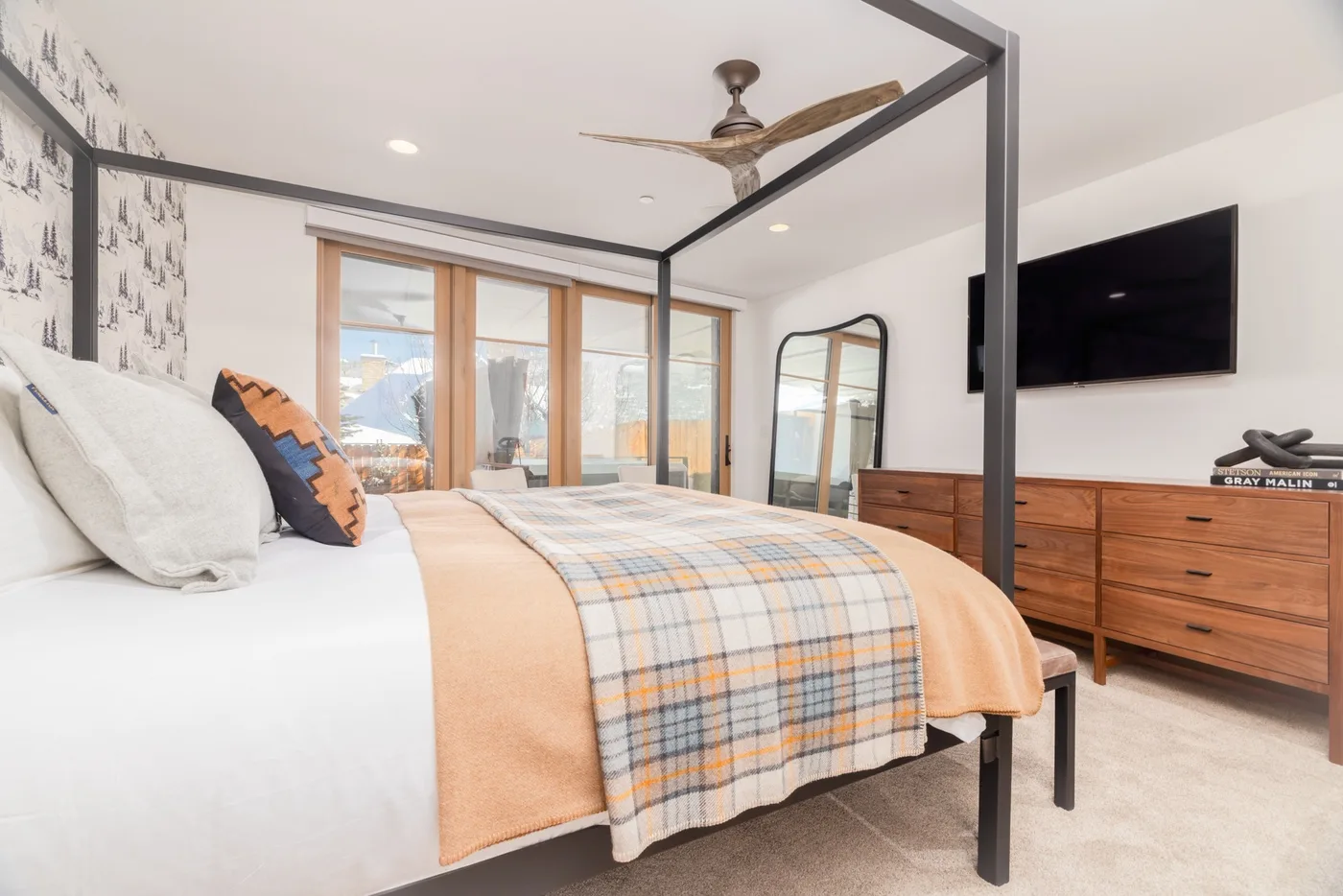 A bedroom with a bed, a wooden dresser, and a television mounted on the wall.