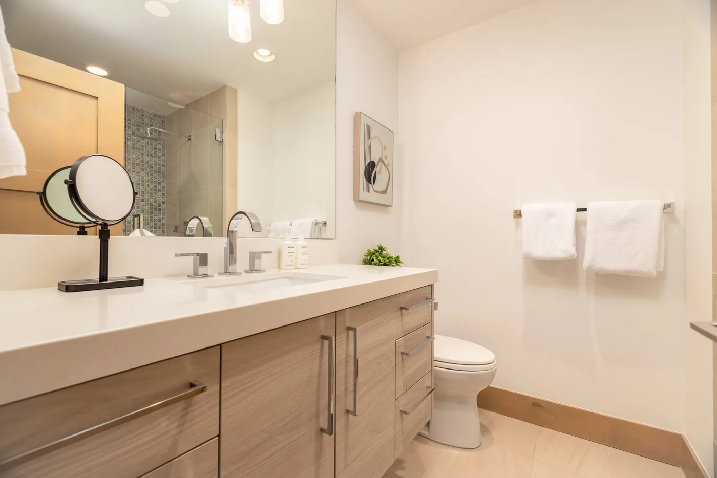 A bright bathroom with a long vanity, mirror, and toilet.