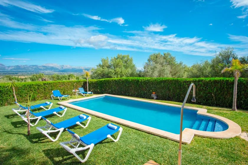 Piscina al aire libre junto a un césped con asientos reclinables.