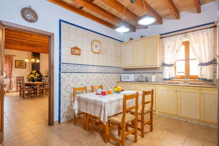 Una cocina con azulejos, mesa de comedor de madera y sillas junto a la encimera.