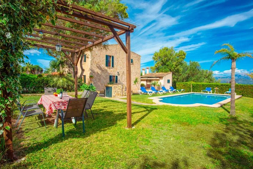 Un patio ajardinado con piscina, asientos al aire libre y una pérgola junto a una casa.