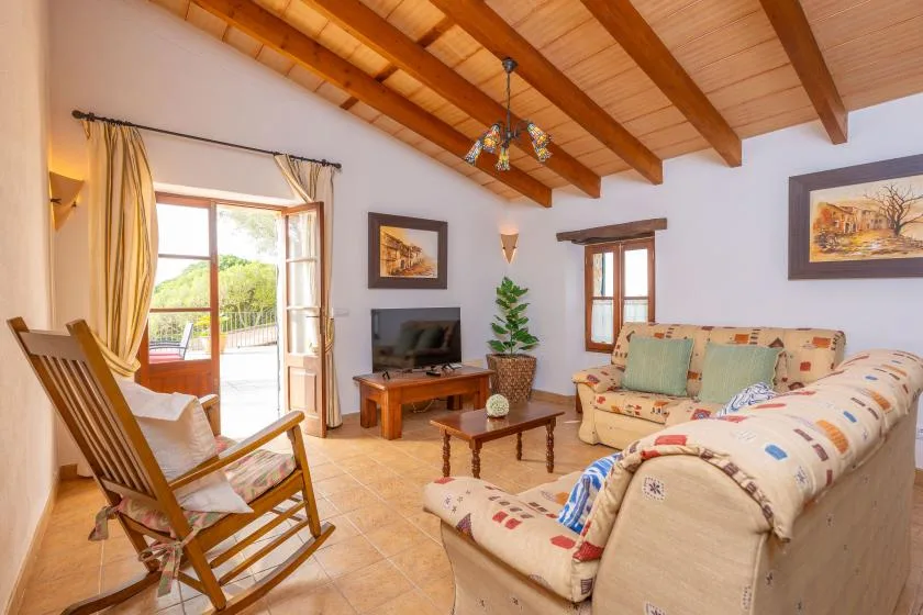 Una sala luminosa con asientos, un televisor y un techo con vigas de madera.