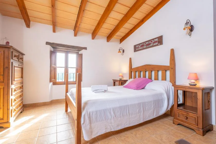 Un dormitorio luminoso con una cama de madera y un techo inclinado de vigas.