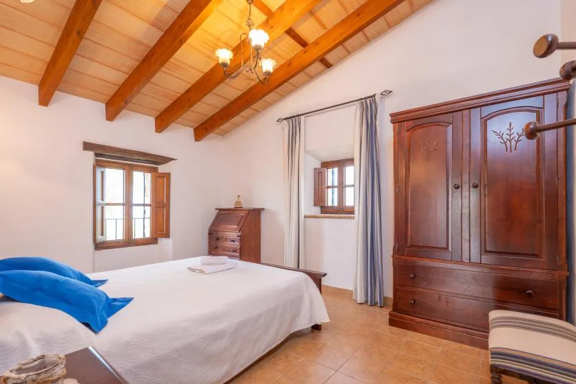 Un dormitorio con una cama, un armario de madera y vigas expuestas en el techo.