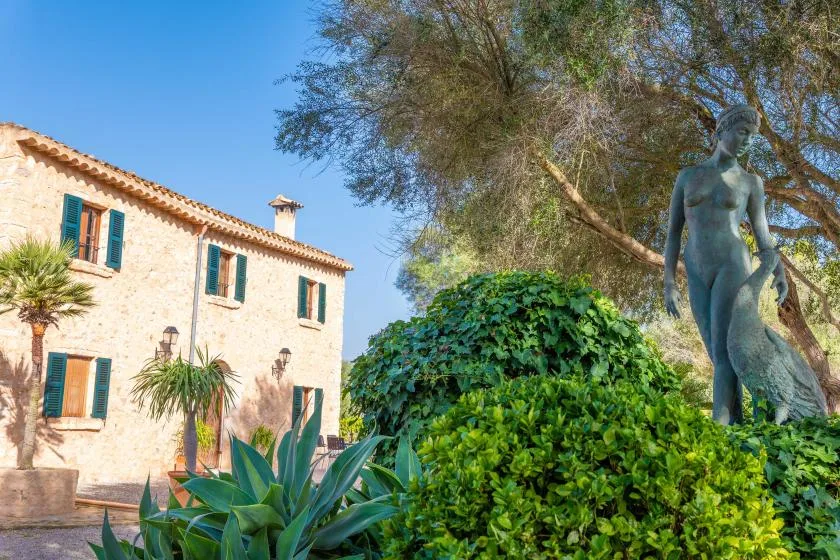 Una casa de piedra está junto a un jardín frondoso con una estatua.