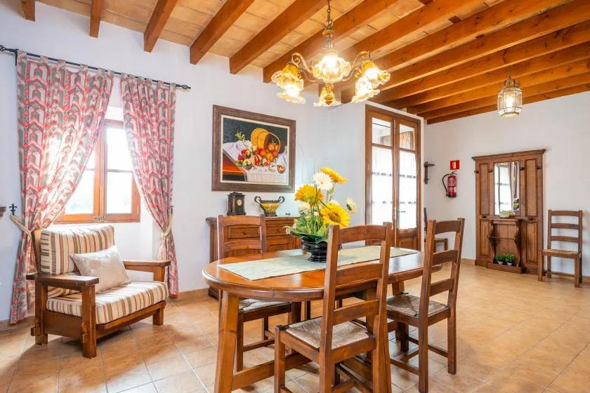 Comedor con una mesa y sillas de madera bajo vigas expuestas en el techo.