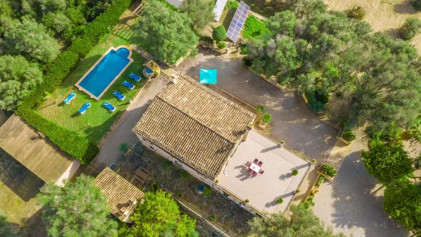 Vista aérea de un edificio con tejado de tejas junto a una piscina y una terraza pavimentada.