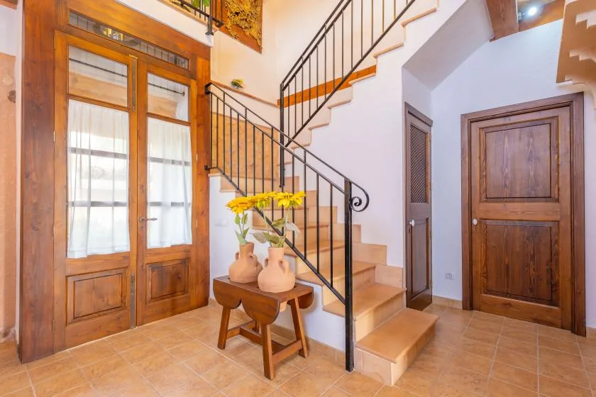 Una escalera interior con barandales negros sube junto a puertas de madera y una mesita.