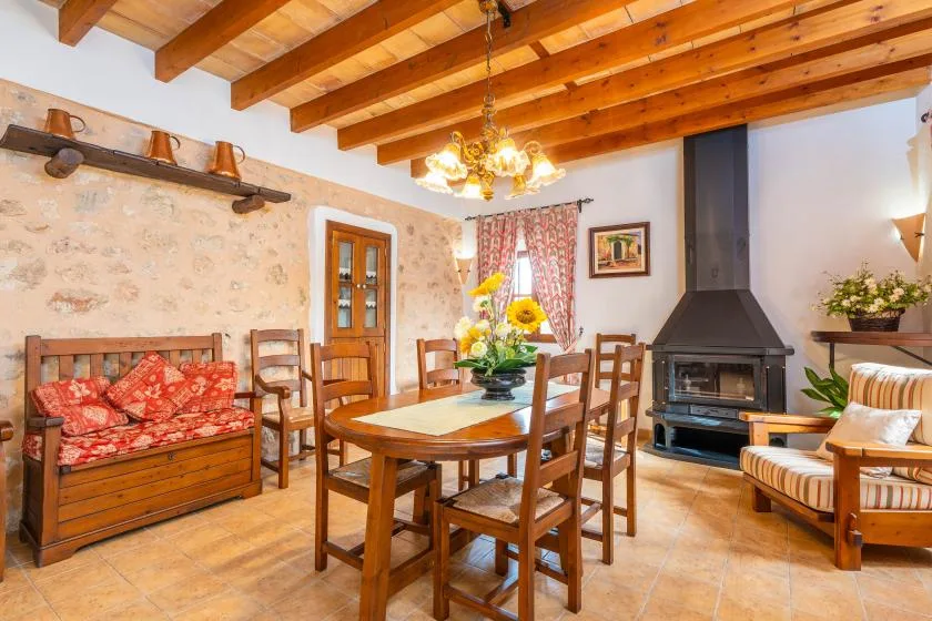 Un comedor con mesa de madera, asientos y una chimenea bajo vigas de techo a la vista.