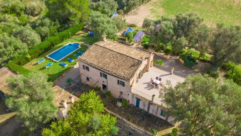 Una vista aérea muestra una casa de piedra con piscina y árboles alrededor.