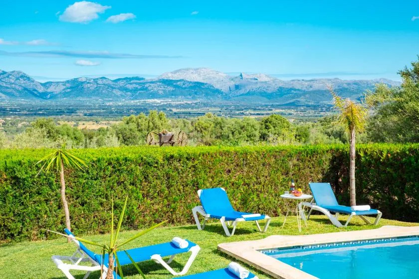 Una piscina y asientos de descanso miran hacia campos verdes y montañas lejanas.