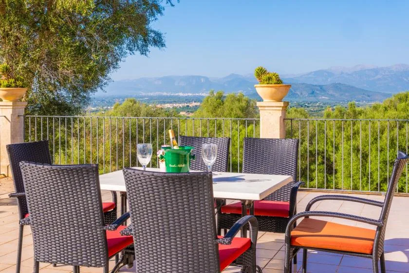 Una zona de comedor al aire libre con asientos tejidos mira hacia un paisaje verde y montañas lejanas.