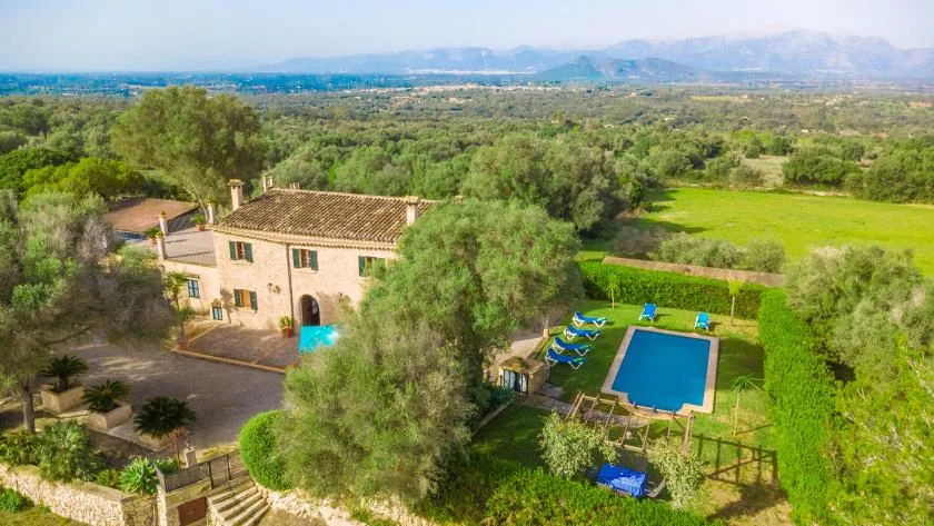 Una casa rural y una piscina están rodeadas de campos verdes y árboles.